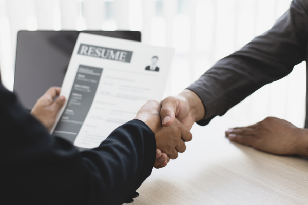 two people shaking hands, one holds a resume