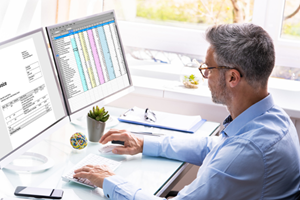 man looking at spreadsheet on computer monitors