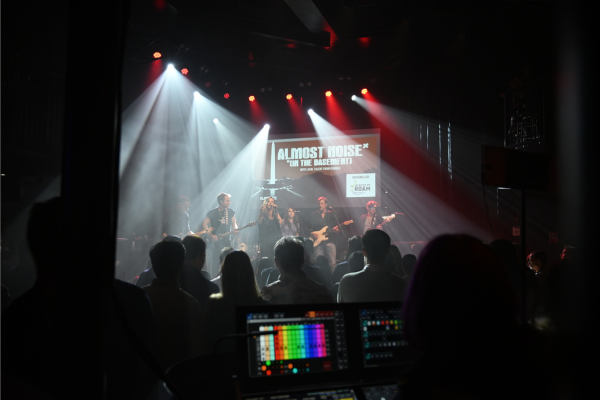 Band on venue stage in background with lighting and audio equipment in forefront.
